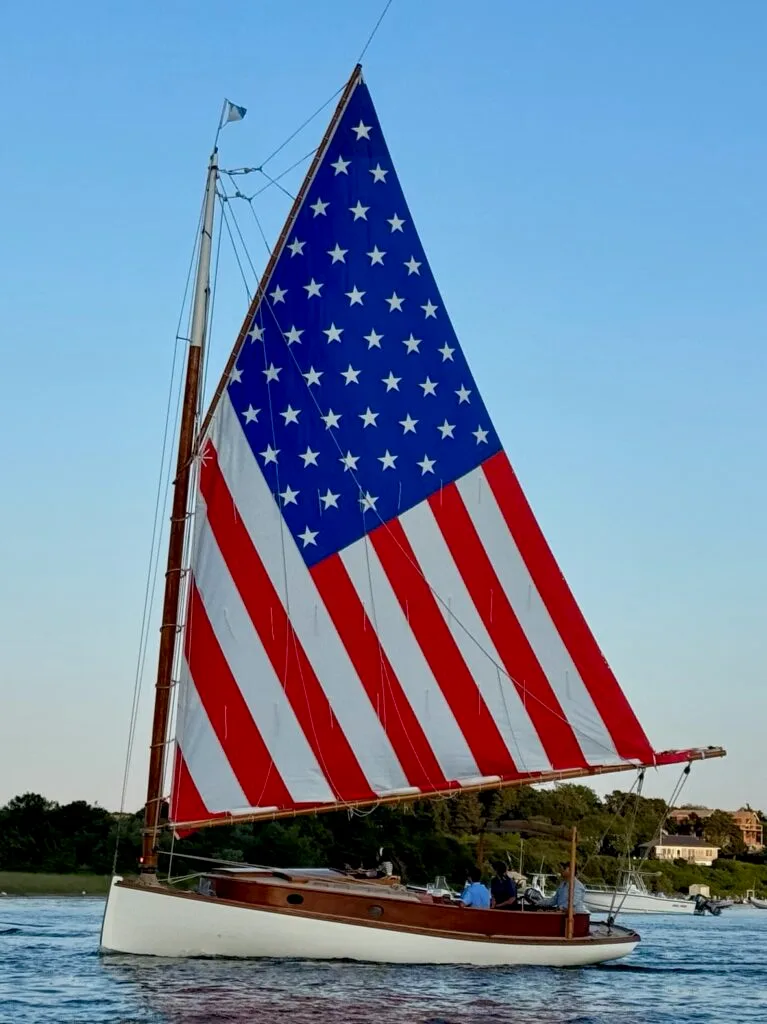 Catboat rigged with American flag sail in Edgartown on 4th of July before the fireworks