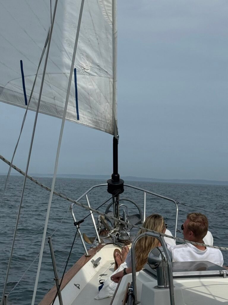 Couple dressed in all white enjoying sailboat ride from the bow.